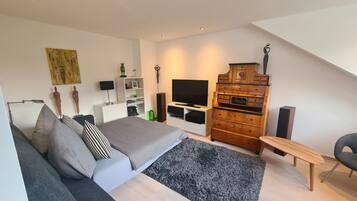 Ein modernes Schlafzimmer mit einem Bett, einem grauen Sofa, einer Holzkommode, einem Fernseher und einem kleinen Tisch.