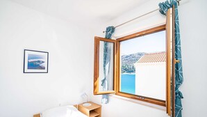 Ein Schlafzimmer mit Bett, Nachttisch, gerahmtem Bild, Fenster mit Vorhängen und Blick auf ein Gebäude und Wasser.