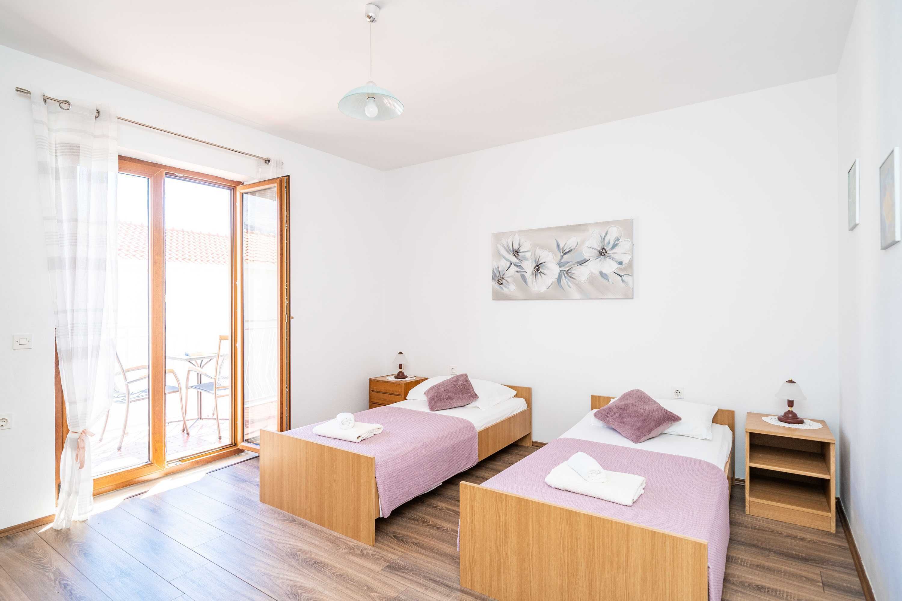 Une chambre avec deux lits, une porte-fenêtre coulissante, un luminaire au plafond et un tableau accroché au mur.