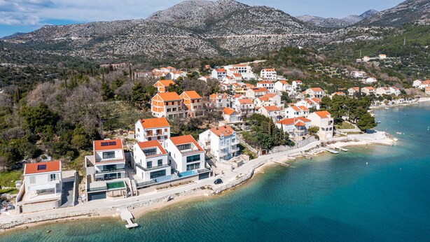 Eine Küstenstadt mit modernen Gebäuden, einem Strand und Bergen im Hintergrund.
