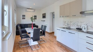 A modern kitchen with white cabinets, a dining area with a black sofa and chairs, and a wooden floor. - Holiday House Chill out Loborika (Marcana)