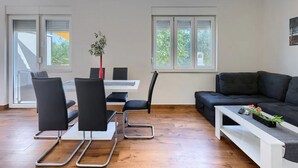 A modern living room with a black sofa, a white coffee table, and a dining area with black chairs and a white table. - Holiday House Chill out Loborika (Marcana)