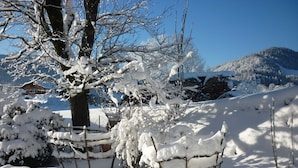 A snow-covered landscape with a house and mountains in the background.