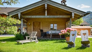 A wooden house with a porch, a bench, a table with flowers, and a potted plant.