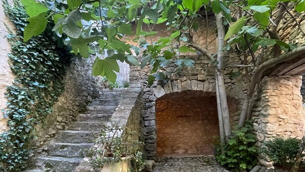 Un escalier en pierre mène à une arche en briques, qui est entourée de verdure et flanquée d’un grand vase.