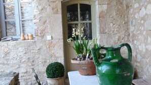 Un mur de pierres rustiques agrémenté d’une fenêtre, une table avec un pot vert et une plante en pot.