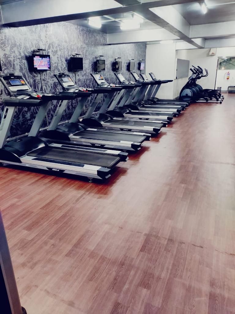 A row of treadmills in a gym with a wooden floor and a patterned wall.