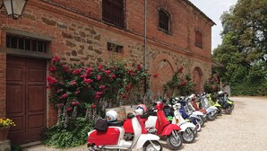 A row of vintage scooters parked in front of a brick building with arched windows and a gravel driveway. - Fattoria Santa Vittoria Apartment "lepre" (Foiano della Chiana)