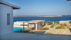 Vistes cap a la costa amb una piscina, mobiliari exterior i una construcció de pedra.