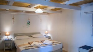 Een net opgemaakt bed met een witte deken en kussens, twee nachtlampjes, een klein nachtkastje en een wandlamp.