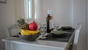 A dining table with a bowl of fruit, a wine bottle, and glasses. - Villa 78 m2 in Agia Irini, 350 Meter to the Beach for 4 Guests With Pool Access! (Paros)