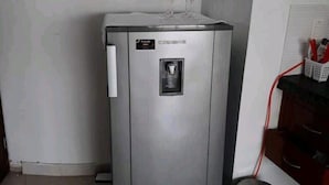 Uma geladeira metálica compacta com um dispensador de água e dois copos de vinho em cima.