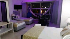 Quarto de hotel com cama, escrivaninha, cadeira, sofá e janela com vista para a cidade à noite.