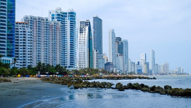 Paisagem costeira com edifícios altos, uma praia de areia e um litoral rochoso.