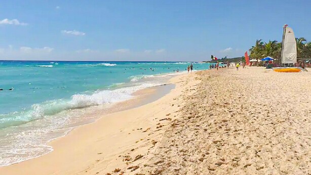 Una playa con agua turquesa cristalina, orilla arenosa y un velero.