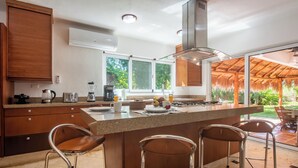 Una cocina moderna con una isla grande, taburetes de bar y vistas a un jardín tropical.