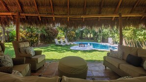 Un espacio al aire libre con mobiliario de mimbre, piscina y abundante vegetación.