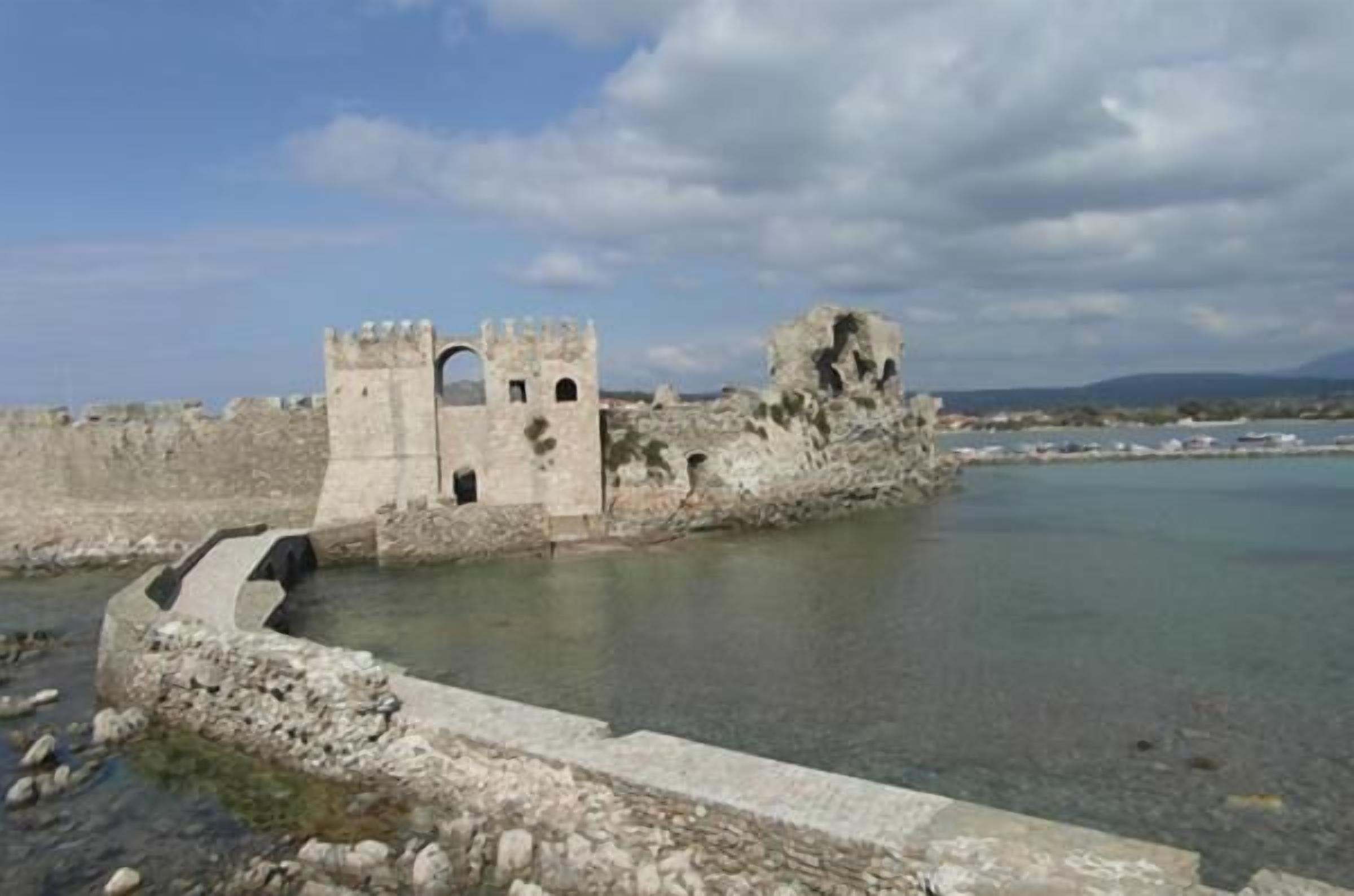 A historical stone structure with a moat, likely a castle ruin, overlooking a body of water.