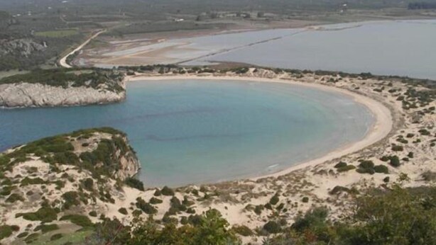 Ett kustlandskap med en sandstrand, en klarblå lagun och klippiga utskjutande partier.