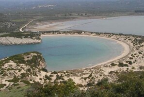 Paisagem costeira com uma praia arenosa, uma lagoa azul cristalina e afloramentos rochosos.