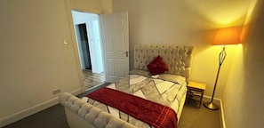 A 2nd bedroom with a tufted headboard, a red throw blanket, and a bedside lamp. - Luxury 2 Bedroom Entire Flat - Self Check in & Check out (Kelty)