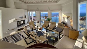 A spacious living room with a large TV, comfortable seating, and a view of the ocean. - Villa Pastorale-360 Degree View-boule Game (Paros)