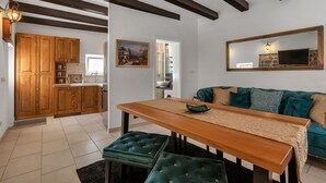 A modern kitchen with wooden cabinets, a dining table with green cushioned benches, and a teal sofa in the living area. - Villa Topolinath Pool (Baska Voda)