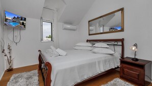 A bedroom with a bed, a bedside table with a lamp, a mirror, an air conditioner, and a window with a view of a building. - Villa Topolinath Pool (Baska Voda)