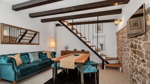 A cozy living room with a teal sofa, wooden dining table, and a staircase leading to an upper level. - Villa Topolinath Pool (Baska Voda)