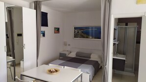 Un dormitori modern amb un llit, taules de nit, un escriptori amb un bol de menjar i un quadre d'un paisatge costaner.