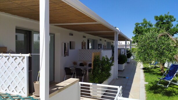 Zona exterior coberta amb taula i caires de pati, una tanca blanca i plantes en testos.