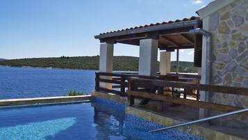 An infinity pool with a stone wall and wooden deck overlooking a body of water.