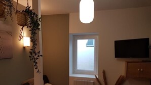 Ein gemütliches Wohnzimmer mit einer Couch, einem Sessel, einem Fernseher, einem Fenster und einer Heizung.
