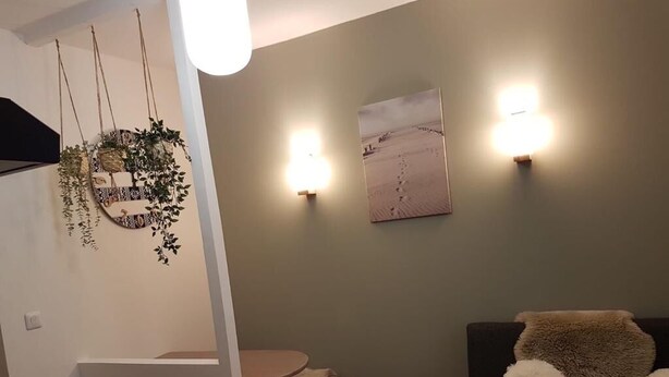 Ein gemütliches Wohnzimmer mit einem runden Tisch, einer Couch mit flauschigen Kissen, einer Wandleuchte und einem gerahmten Bild.