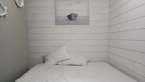 Ein kleiner Raum mit weißen Wandverkleidungen, einem Bett, einem Wandbild und einer Deckenleuchte.