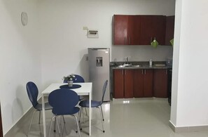 A compact kitchen with a refrigerator, a sink, and wooden cabinets. There is a dining table with blue chairs. - Bright Apartment at Punta Cana Wifi-ac-elect-iron-parking (Punta Cana)
