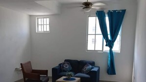A room with a dark blue sofa, a wooden chair, a small wooden table, and a ceiling fan. - Bright Apartment at Punta Cana Wifi-ac-elect-iron-parking (Punta Cana)