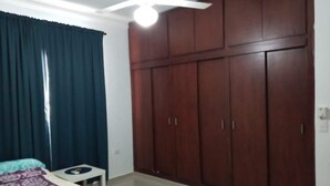 A bedroom with a bed, a small table, a wardrobe, and a ceiling fan. - Bright Apartment at Punta Cana Wifi-ac-elect-iron-parking (Punta Cana)