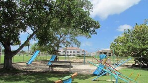 A playground with swings and slides, a bench, and a building in the background. - Bright Apartment at Punta Cana Wifi-ac-elect-iron-parking (Punta Cana)