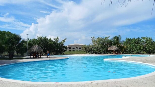 A large swimming pool with a thatched-roof structure nearby. - Bright Apartment at Punta Cana Wifi-ac-elect-iron-parking (Punta Cana)