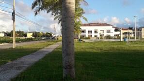A pathway leading to a building with a basketball court, surrounded by greenery and utility poles. - Bright Apartment at Punta Cana Wifi/ac/elect/iron/parking (Punta Cana)