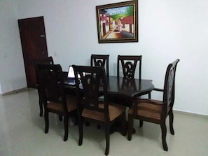 A dining area with a dark wooden table and six chairs. A painting hangs on the wall above the table. - Bright Apartment at Punta Cana Wifi/ac/elect/iron/parking (Punta Cana)