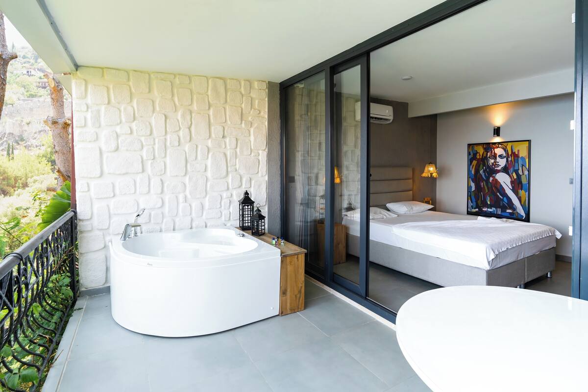 Une chambre moderne dotée d’un grand lit, d’une salle de bain entièrement vitrée et d’un balcon avec un jacuzzi.