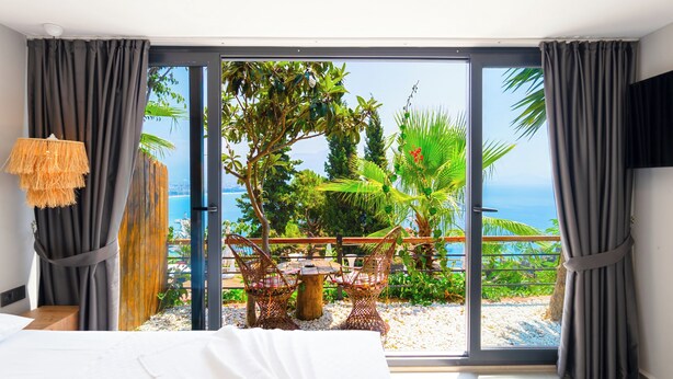 A bedroom with a large sliding glass door leading to a balcony with a view of the sea and a garden. - Castle Boutique Hotel Alanya (Alanya)