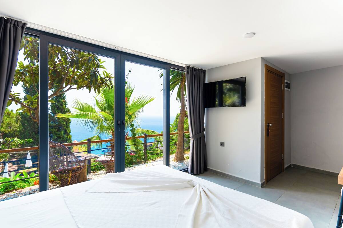 Une chambre dotée d’un grand lit, d’un téléviseur fixé au mur et offrant une vue sur une piscine et un espace verdoyant.