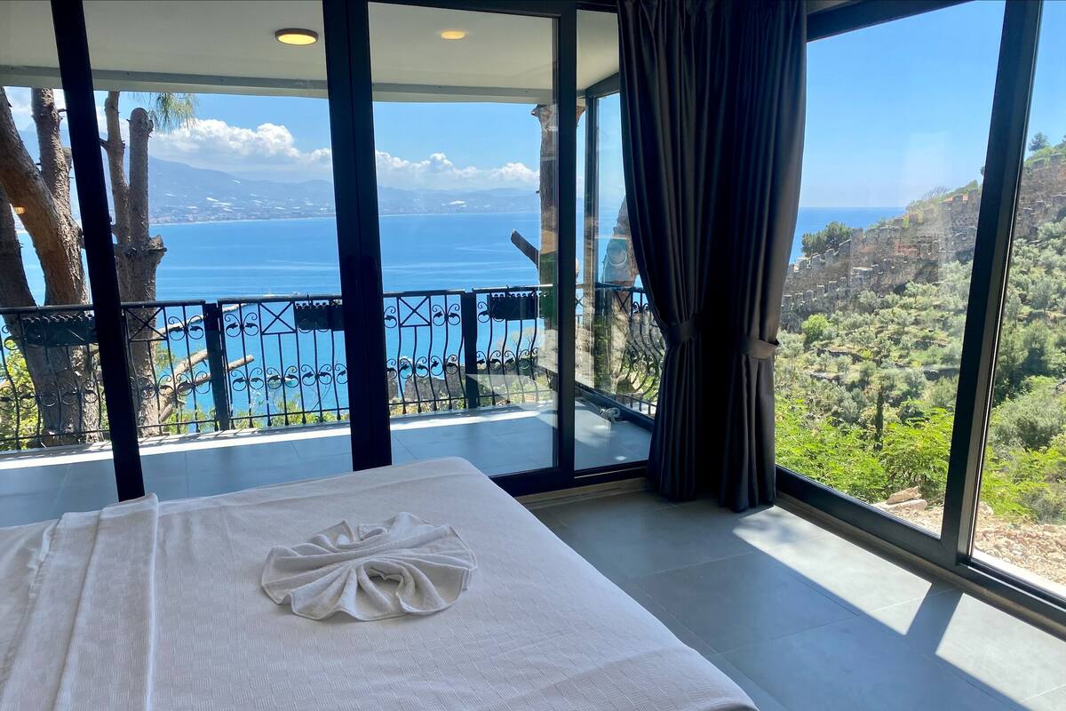 Une chambre dotée d’une grande fenêtre donnant sur un paysage magnifique, avec vue sur la mer et les montagnes.