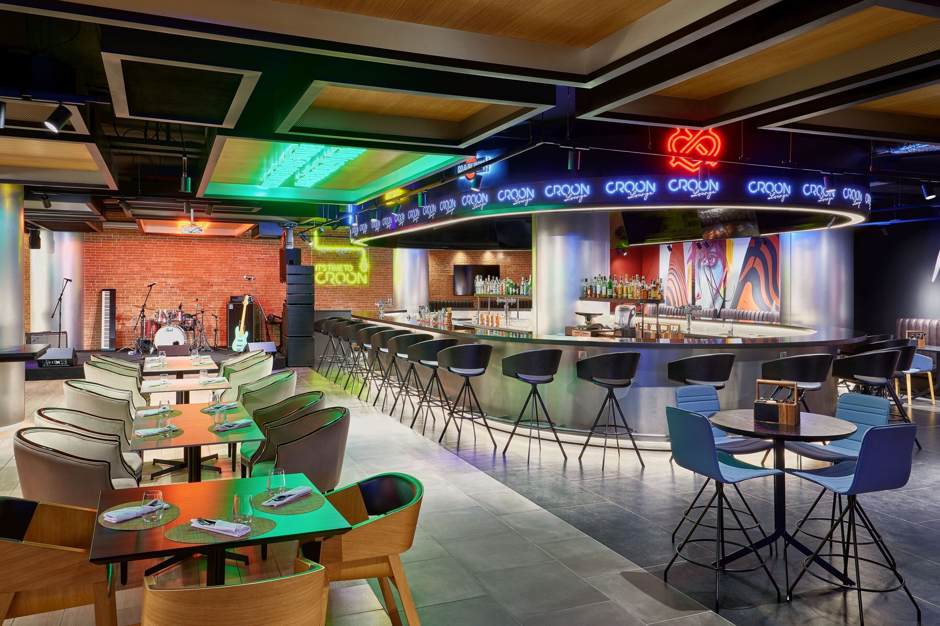 A modern bar area with multiple seating options, a stage for live performances, and a neon sign reading "Crown."