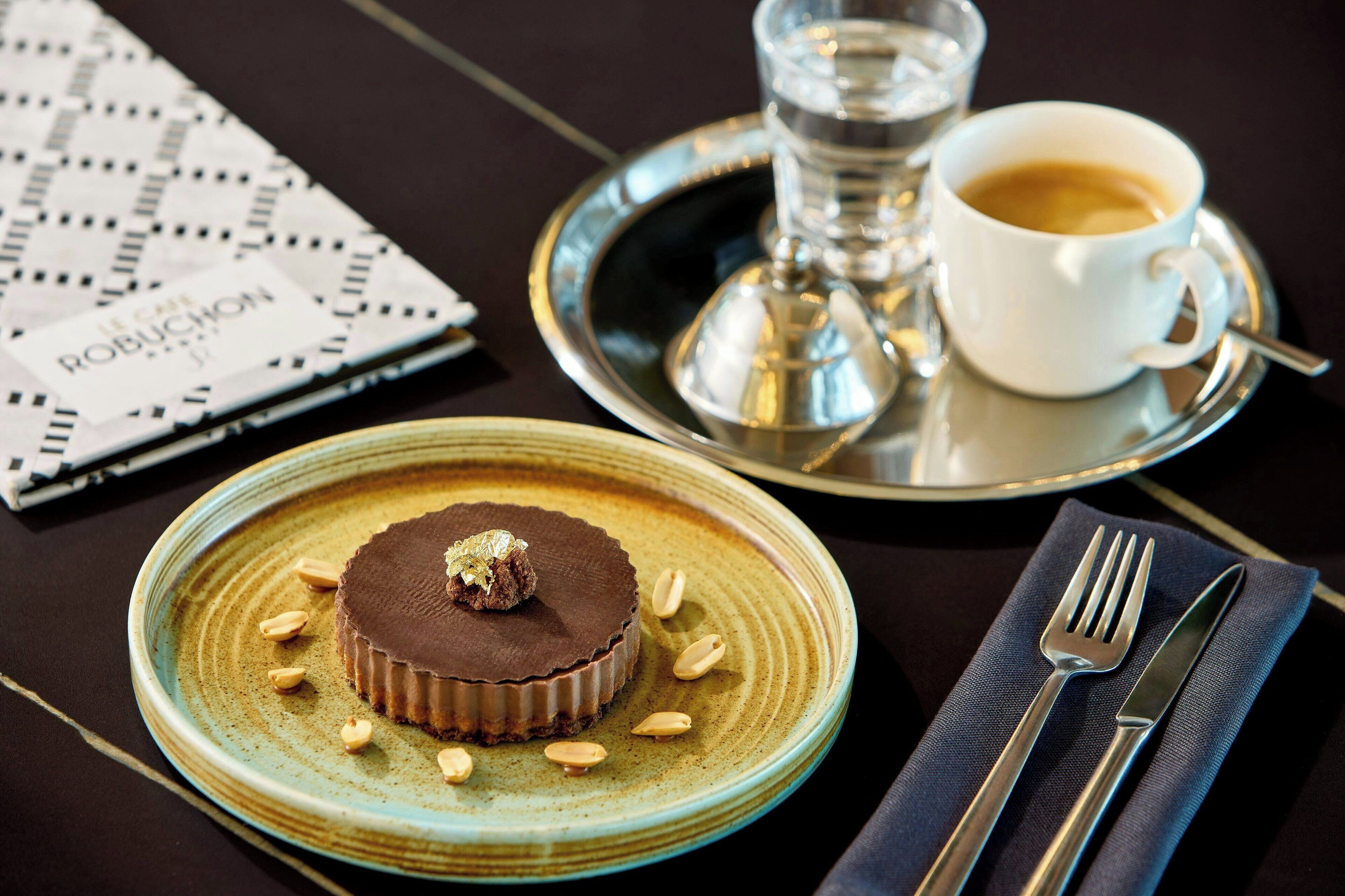 Een nagerechtenbord met chocoladetaart, een kop koffie en een menukaart op een tafel.