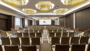 A conference room with rows of chairs, a large screen at the front, and modern chandeliers.