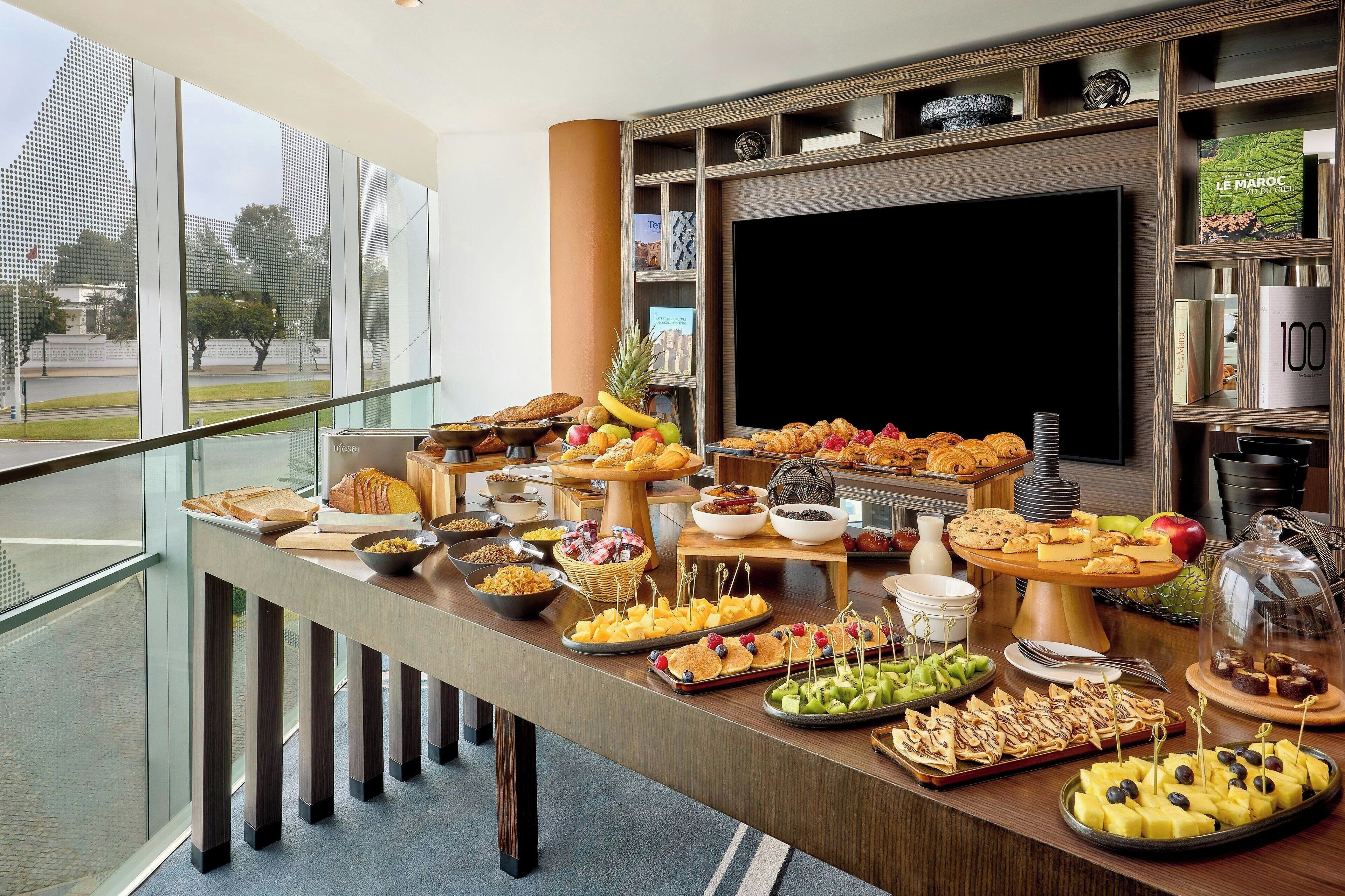 Una mesa de buffet con diferentes alimentos y un televisor al fondo.